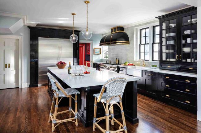 Black glossy kitchen cabinets with cherry wood floors, white marble tile, and gold and wicker accents