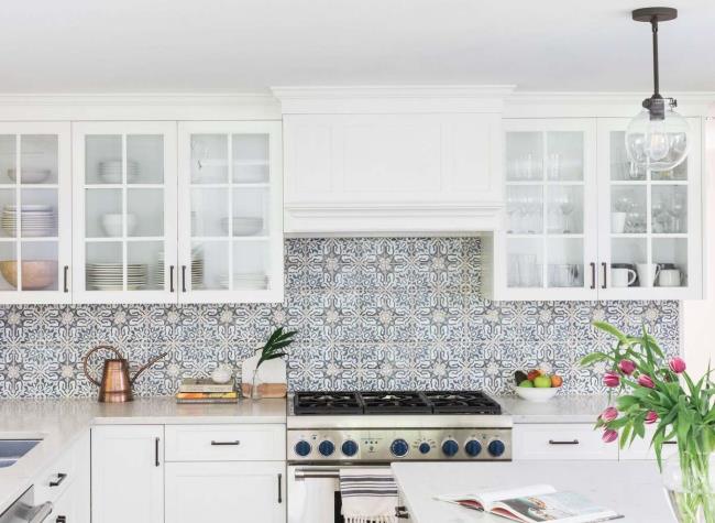 Glass front white cabinets in front of a Spanish tile backsplash