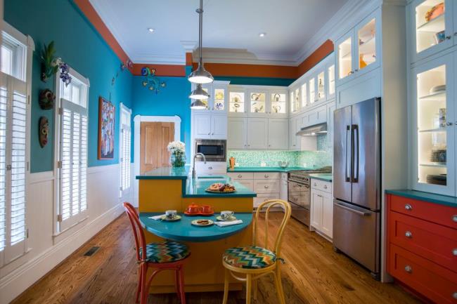 Tropical eat-in kitchen with bright blue walls and small blue table with red and yellow chairs.