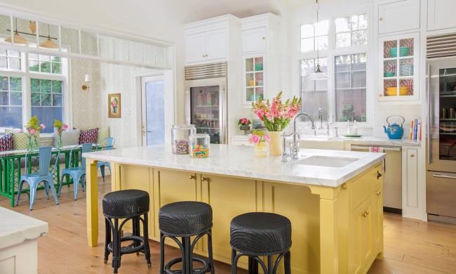 Yellow cabinets, white counters, and three black bar stools in a kitchen.