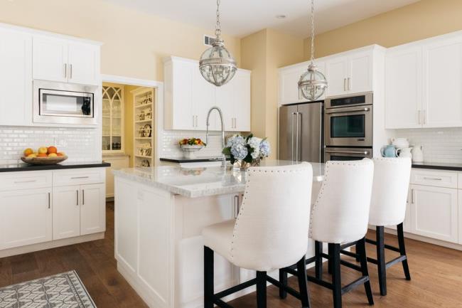 French country stylized kitchen with white cabinets, vintage white chairs hanging globe lights