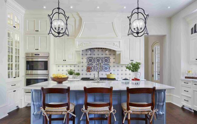 Crisp French country kitchen with blue island, hanging pendant lights, blue tile on the walls, and three wooden chairs.