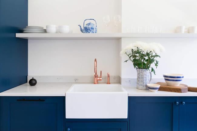 Blue kitchen cabinets with white farmhouse sink and copper faucet.