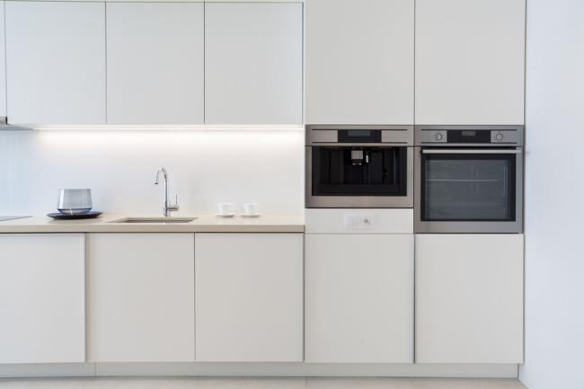 Small modern white kitchen with wall oven next to built-in wall espresso maker.